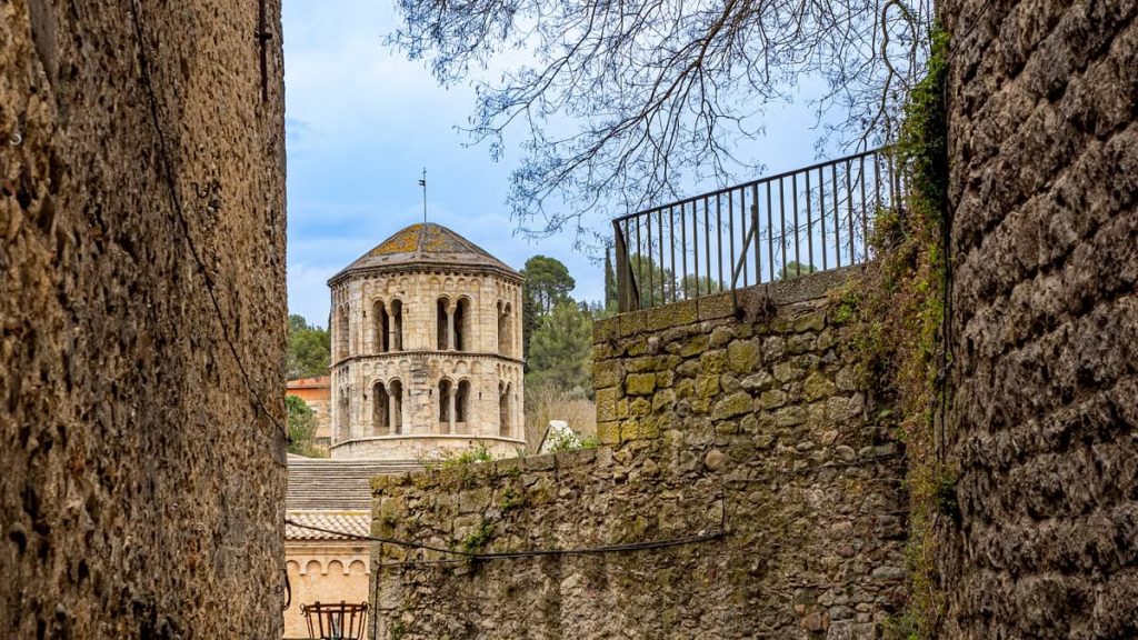 A glimpse of the historic Monastery of Sant Pere de Galligants in Girona through ancient city walls.